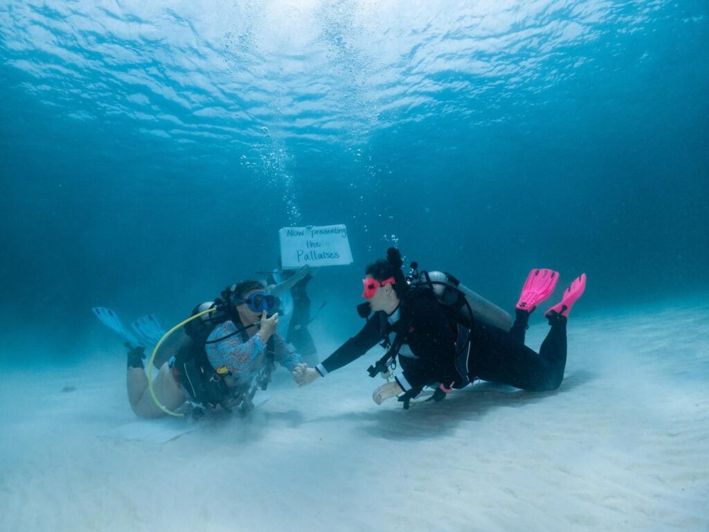 Mariya and Sam Pallais holding hands on the sandy sea floor