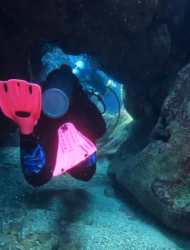 A diver in pink fins coming through a cave opening