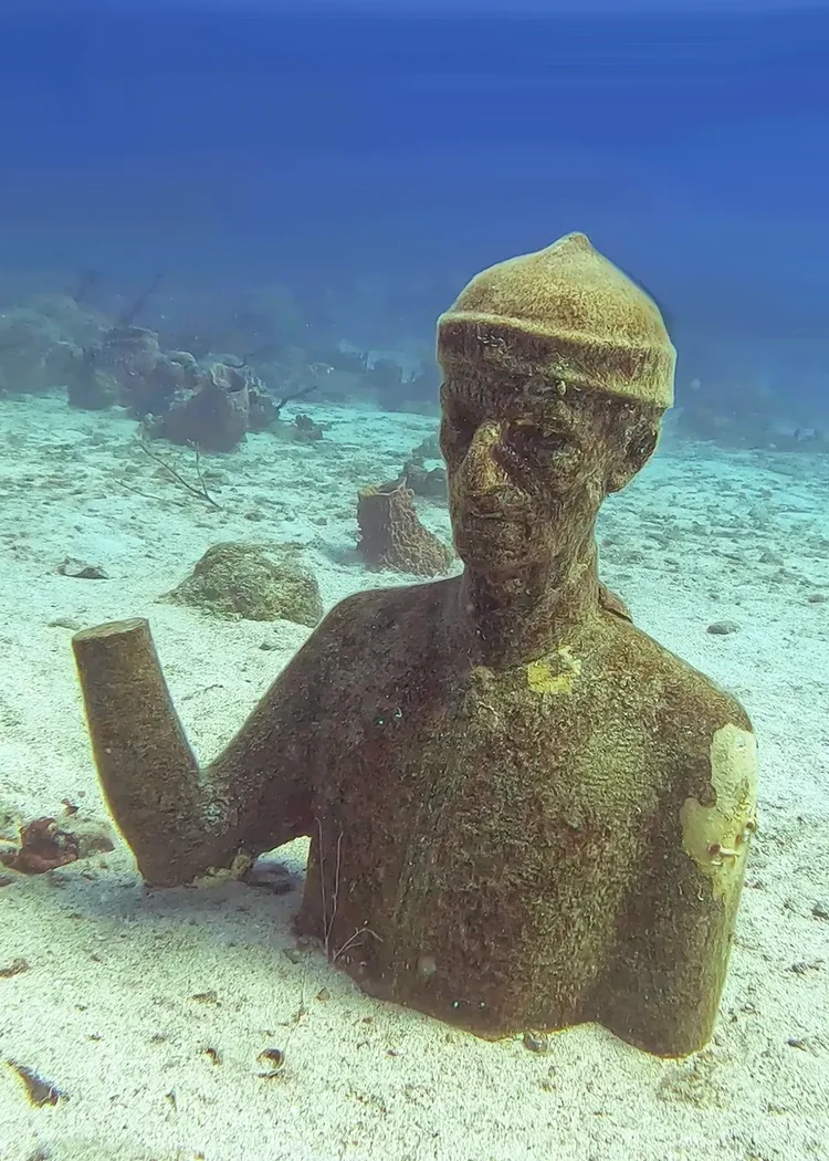 An underwater statue of a man in a knit cap on the sand